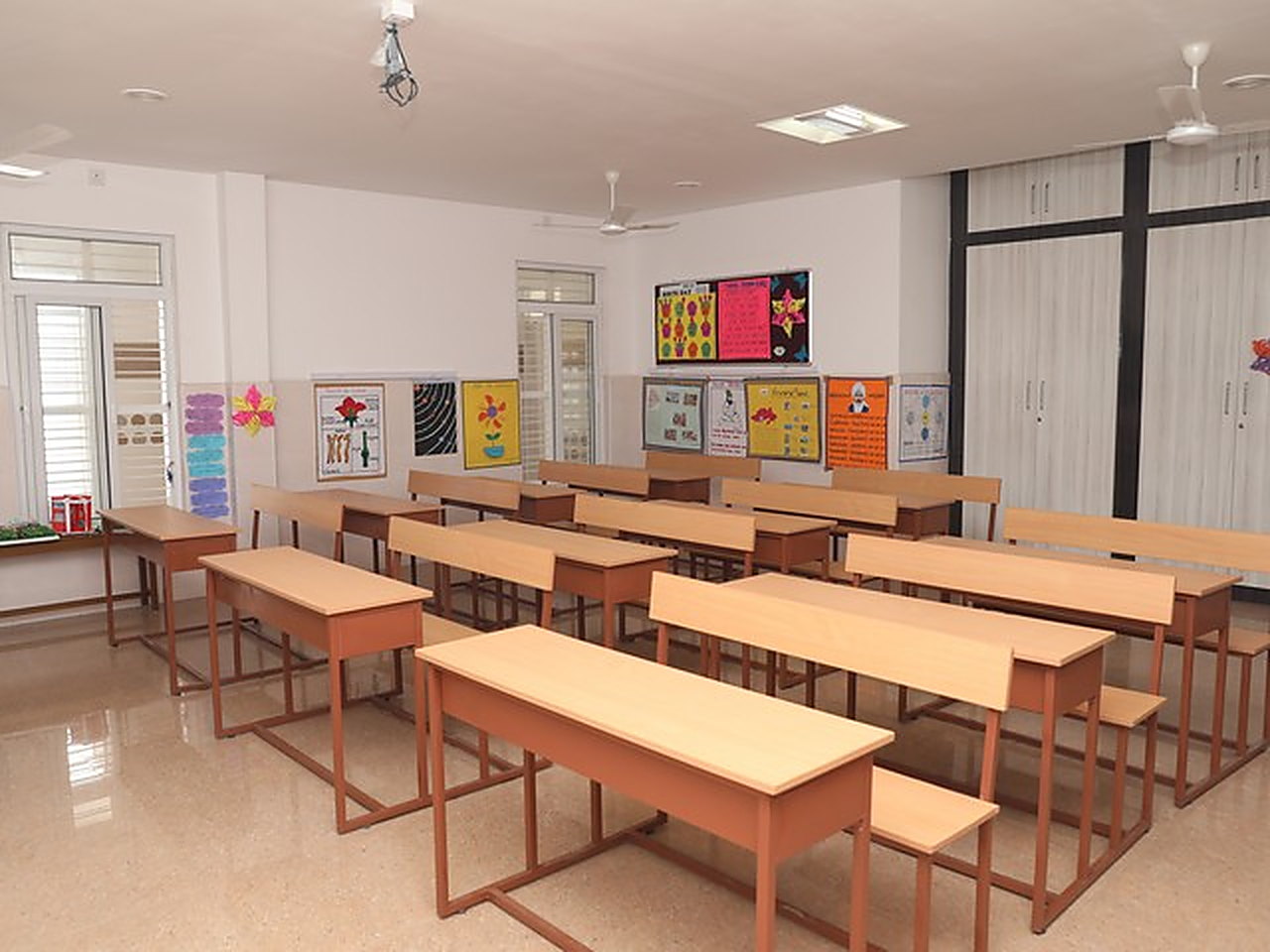 A classroom of wooden desks, with charts on the display boards